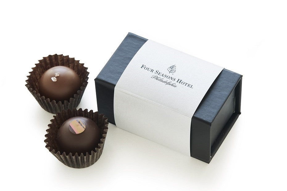 Two chocolate truffles in dark paper cups with a Four Seasons Hotel branded box on a white background