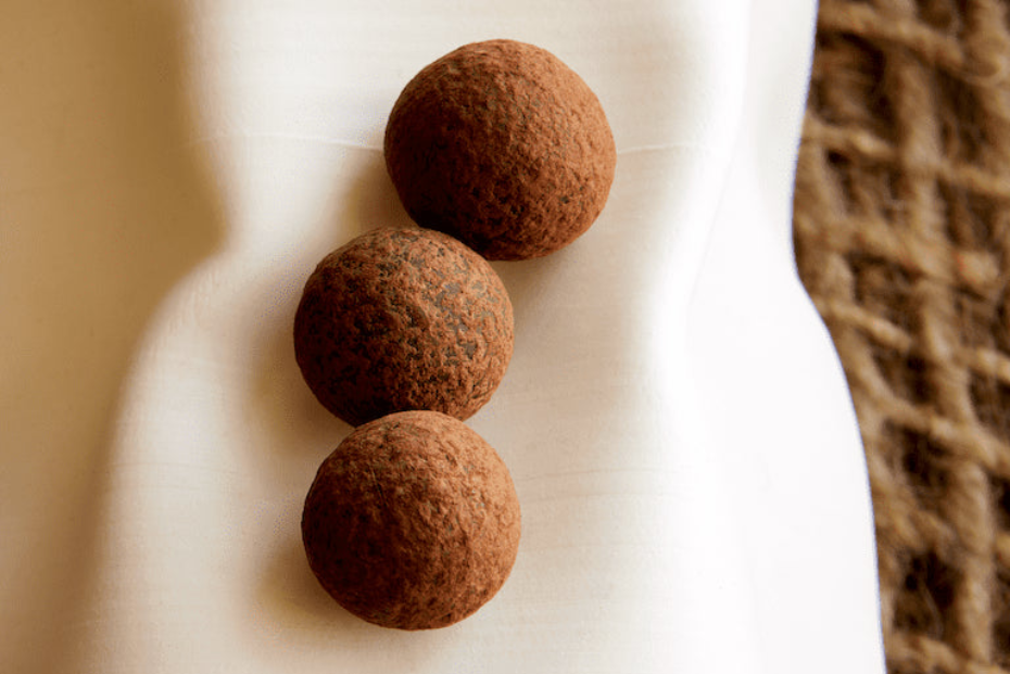 Three chocolate truffles on a white marble surface with a woven mat in the background.