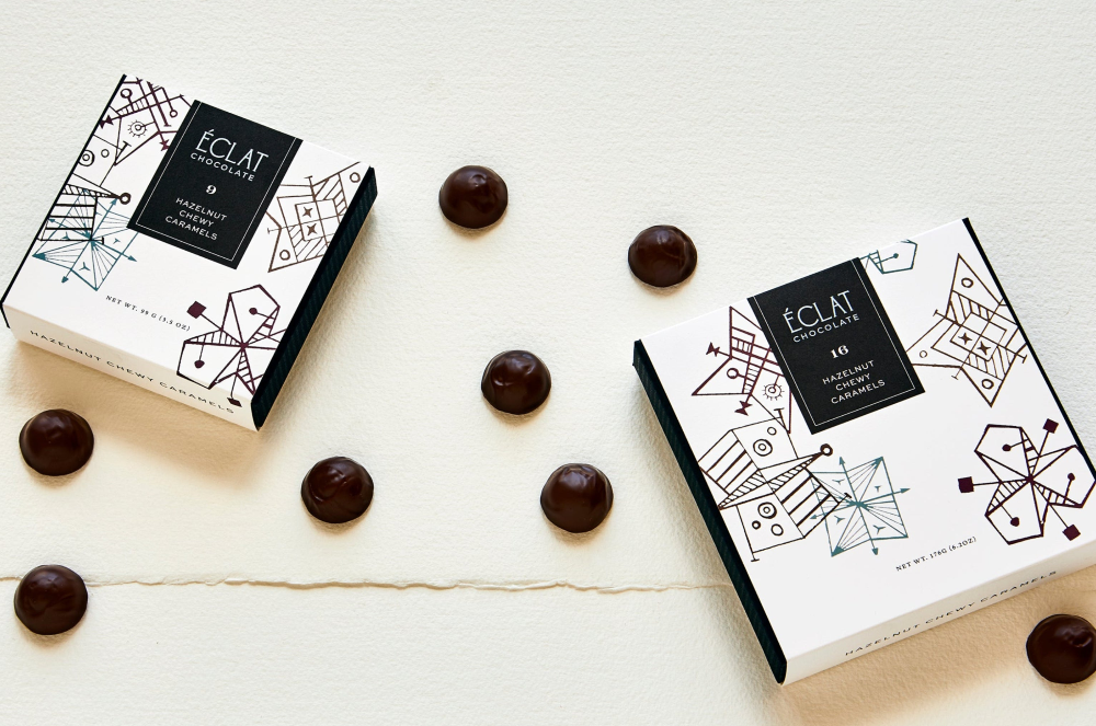 Two boxes of 'Eclat' chocolates on a white surface with chocolate truffles around them.